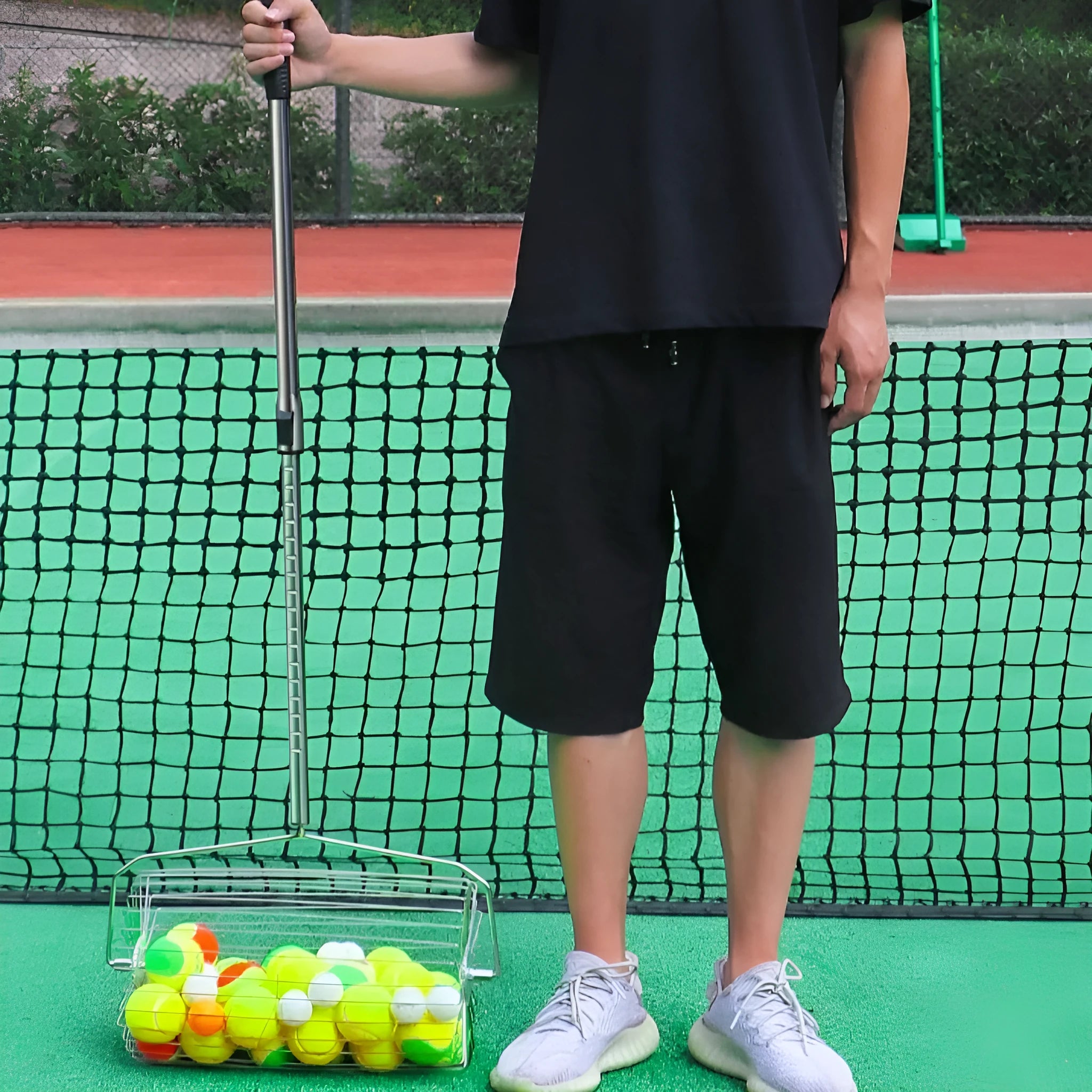 Stainless steel roller tennis ball picker with adjustable head on a court surface.