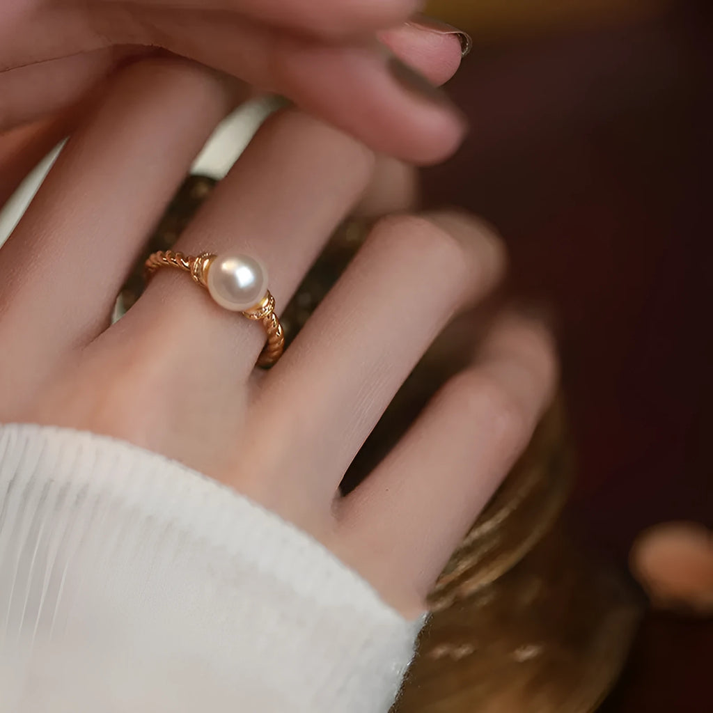 Antique-style twisted copper ring with a central white pearl, shown on a finger, adjustable band visible.