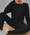 A woman wearing a black sunken stripe two-piece loungewear set, consisting of a regular-sleeve top and elasticated waist trousers.