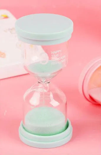Handmade glass sand timer in blue colour showing sand flowing, on a wooden desk.