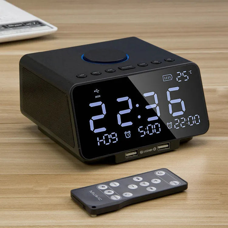 Black and white wireless alarm clock speaker with digital display, twin speakers, and a remote control on a wooden surface.