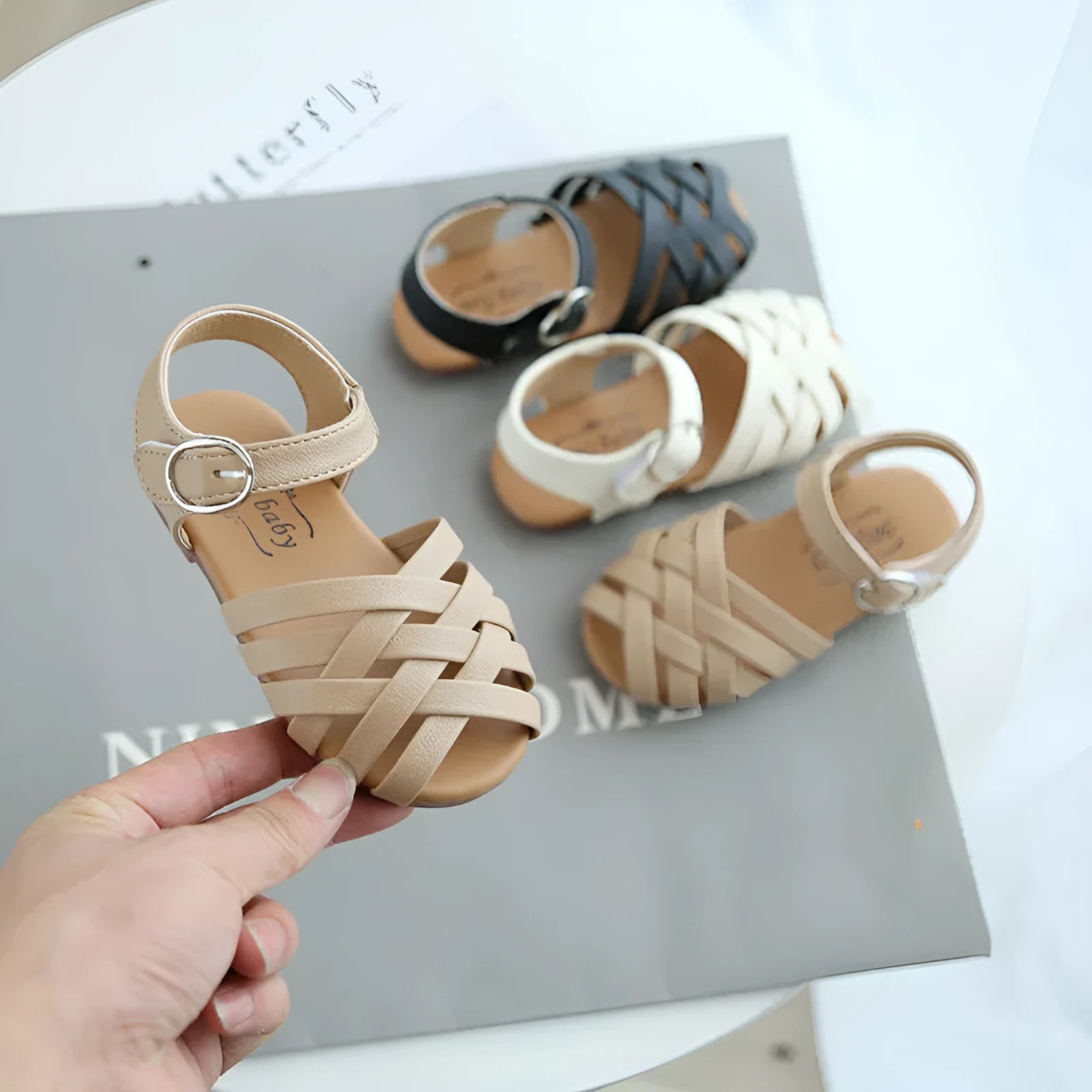 Kids buckle-toe soft sole woven sandals in white, black, and pink on a light background