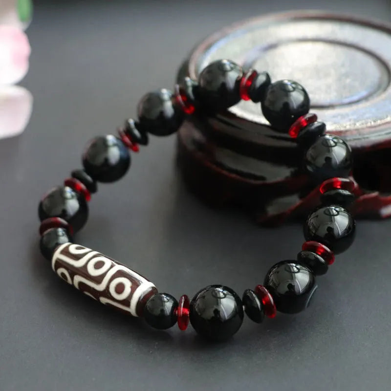 Hand-woven black agate dzi bead bracelet with geometric chalcedony beads on a wrist.