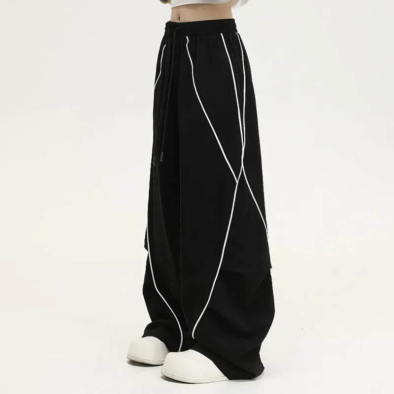 Black sports trousers with white stripes, showing wide-leg loose fit and mid-waist design.