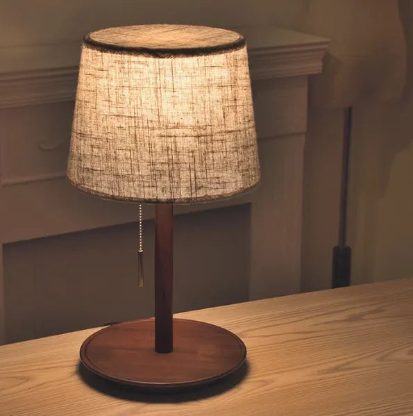 Walnut-coloured solid wood bedside lamp with a white cloth shade on a wooden surface.