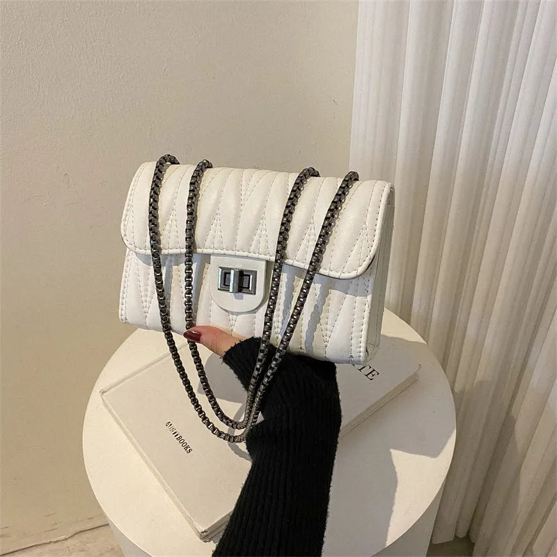 Small beige textured diamond pattern PU women's handbag with a soft handle on a table.