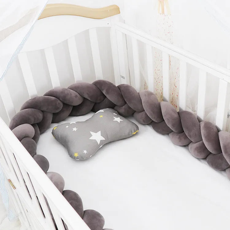 Close-up of a grey braid knot pillow cushion cot bumper fitted around white crib rails.