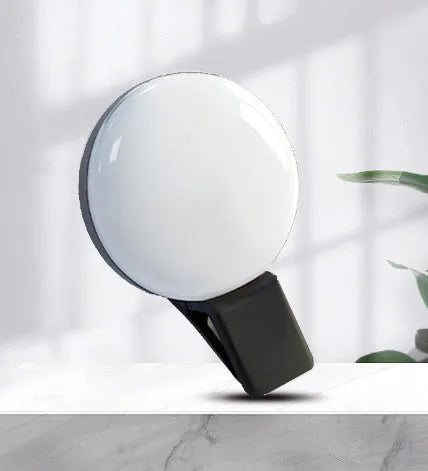 Round USB rechargeable LED fill light attached to a mobile phone for selfies.