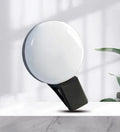 Round USB rechargeable LED fill light attached to a mobile phone for selfies.