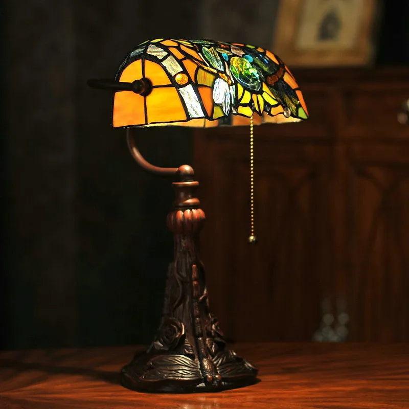 Colourful Tiffany-style stained glass table lamp with resin base on a wooden desk.