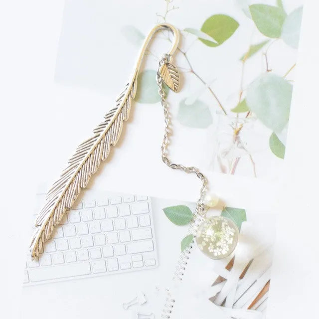 Flat metal bookmark with dried flower inside, showing 12cm length, on an open book.