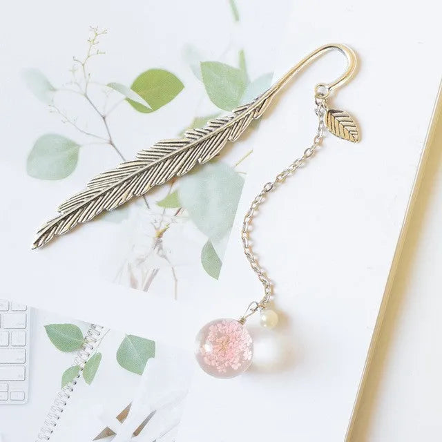 Flat metal bookmark with dried flower inside, showing 12cm length, on an open book.