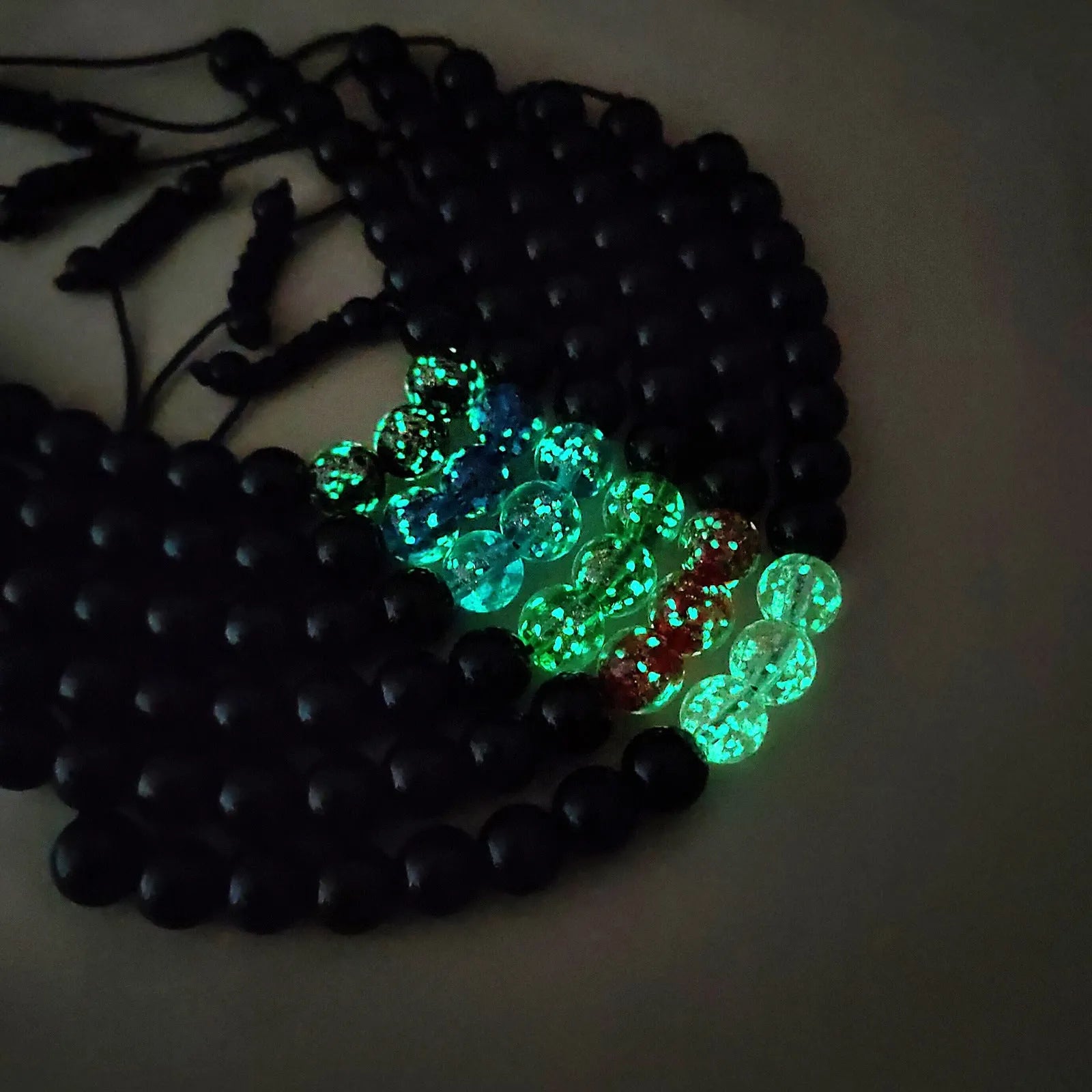 Adjustable luminous glass bead bracelet in geometric shapes on wrist showing elastic cord threading