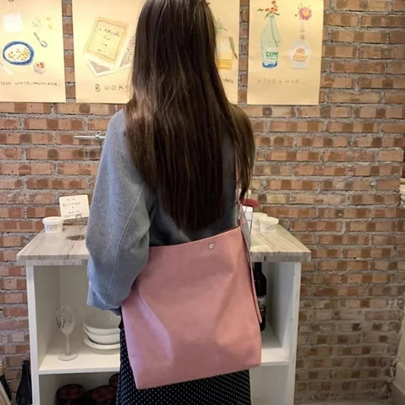 Corduroy one-shoulder messenger bag in pink on a table, showing adjustable strap and structured shape.