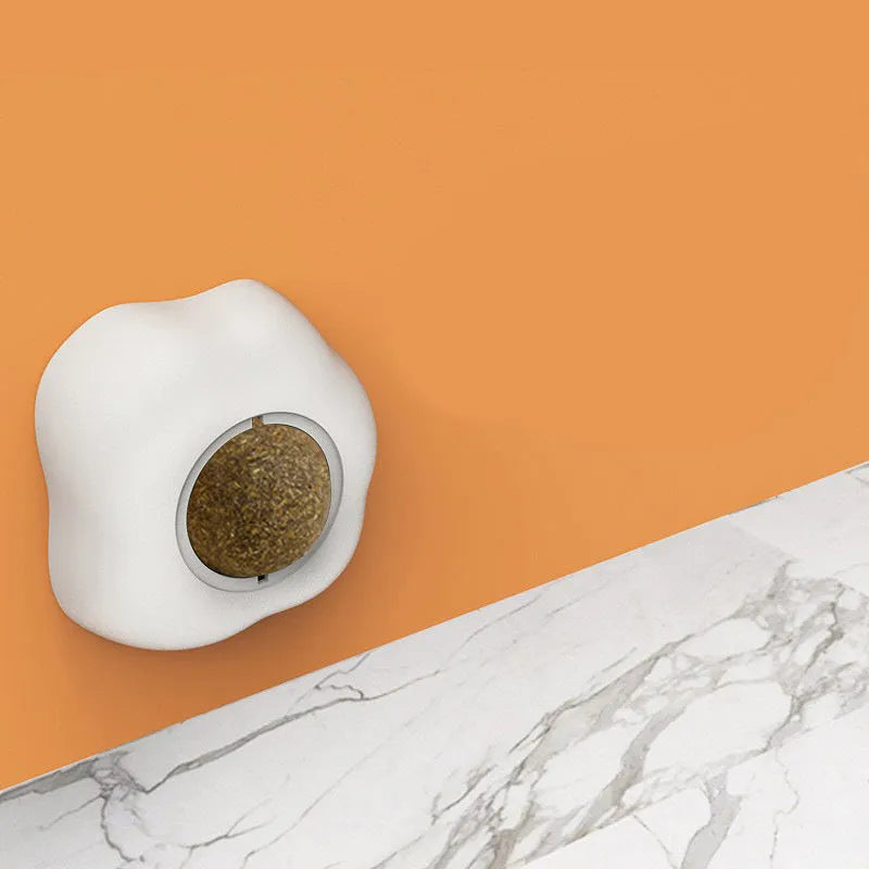 Catnip ball toy with adhesive backing attached to wall, showing cat head shape design