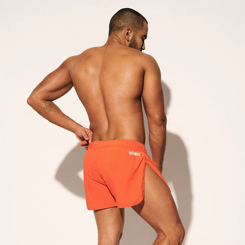 Men's loose-fit polyester beach shorts in orange, fluorescent green, and black on a size chart background.