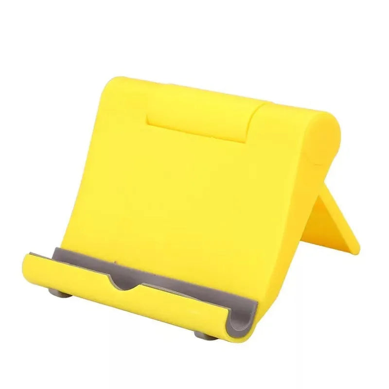 Black PE folding tablet stand holding a mobile phone at an adjustable viewing angle on a wooden desk.