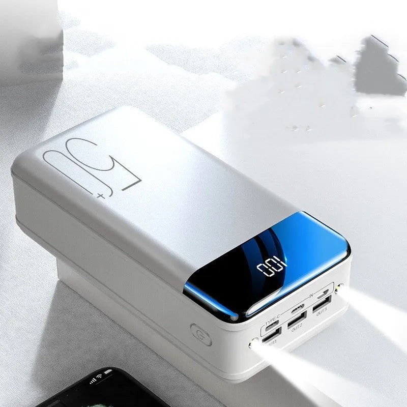 Black and white large 50000mAh portable power bank with multiple USB ports, showing scale next to a smartphone.