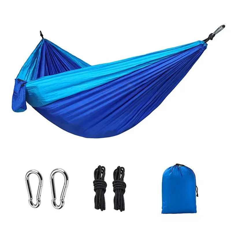 Blue parachute nylon camping hammock hung between two trees, showing its full 270cm length and attachment carabiners.