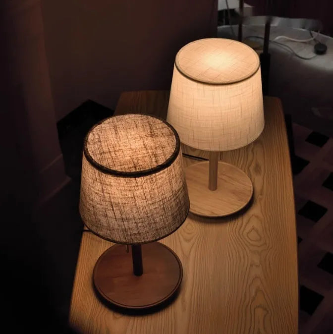 Walnut-coloured solid wood bedside lamp with a white cloth shade on a wooden surface.