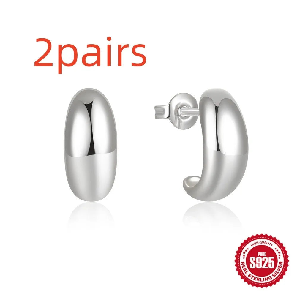 Close-up of a glossy C-shaped sterling silver stud earring on a gold background.