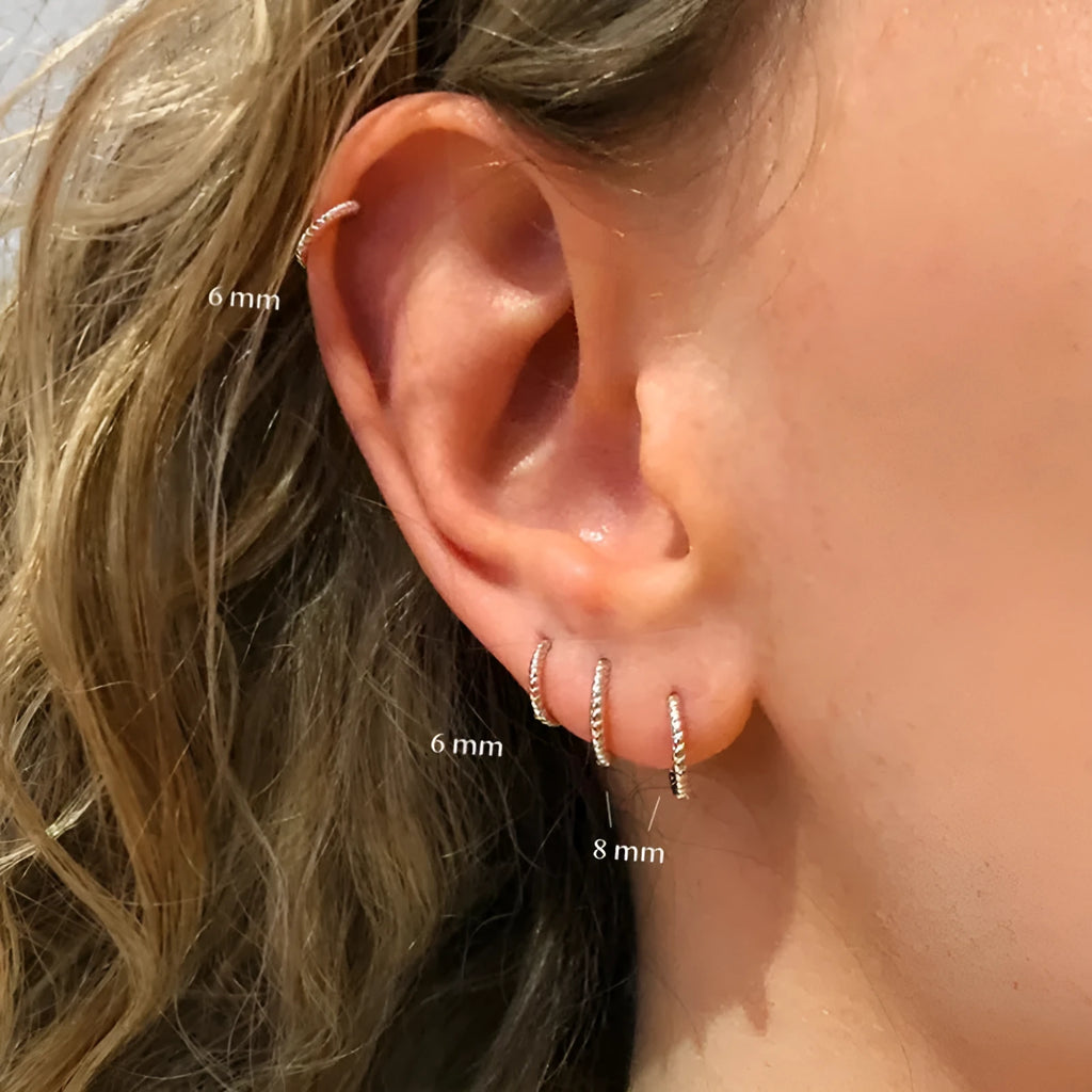 Close-up of a twisted sterling silver round hoop earring in gold colour, showing geometric design.