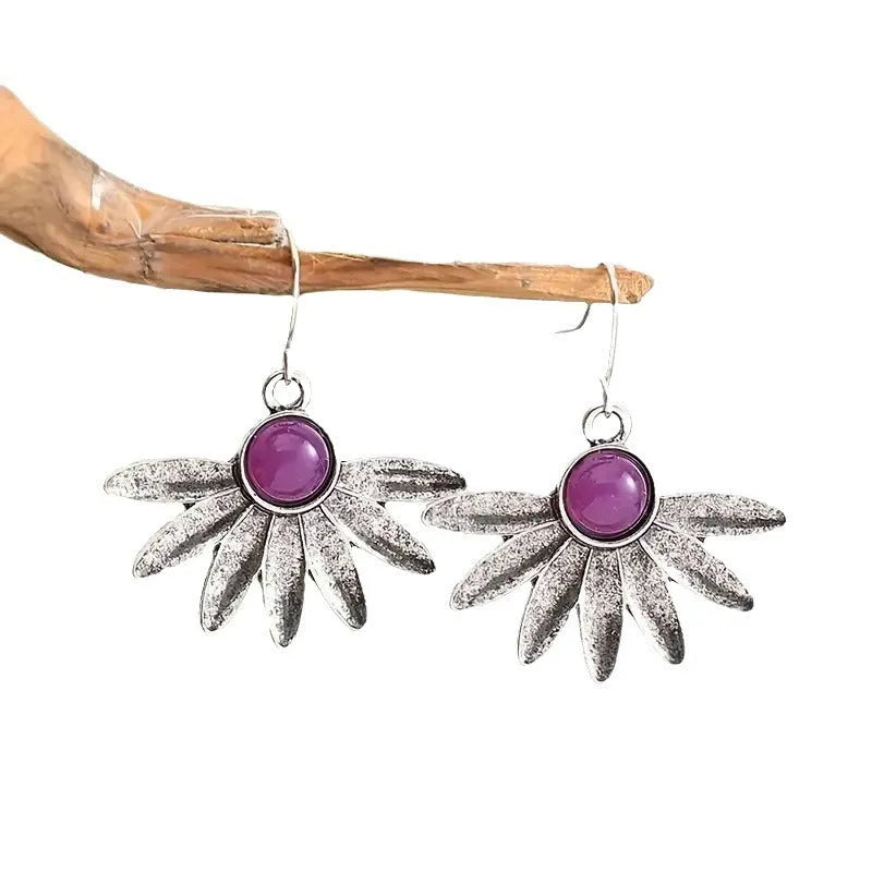 A pair of purple resin bohemian earrings with alloy details and animal or floral modelling on a white background.