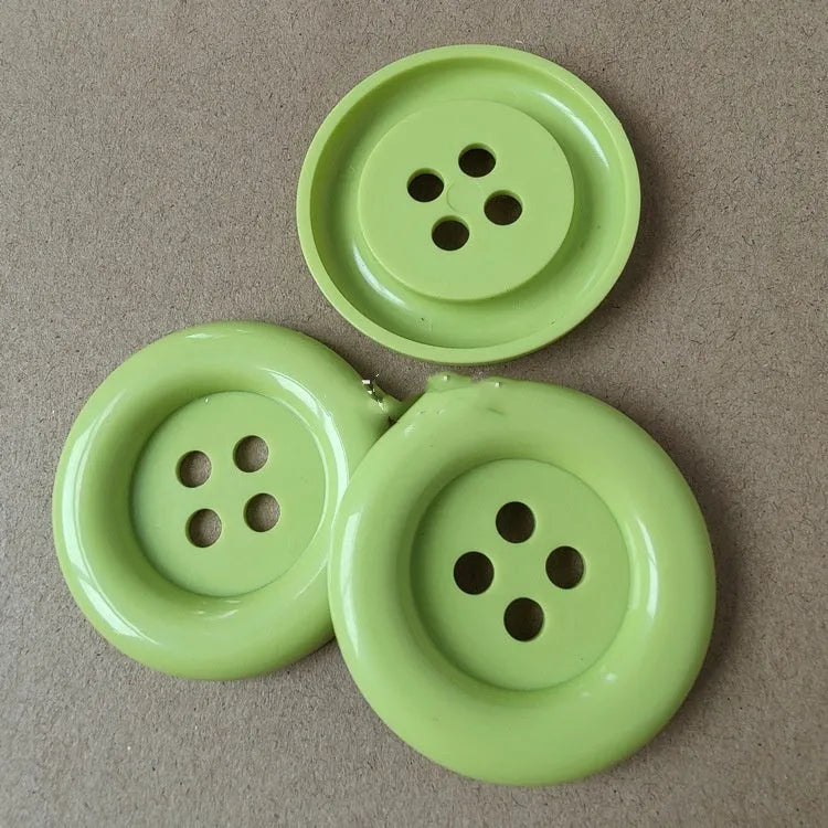 Oversized round edge plastic button with four holes in various colours and diameter sizes