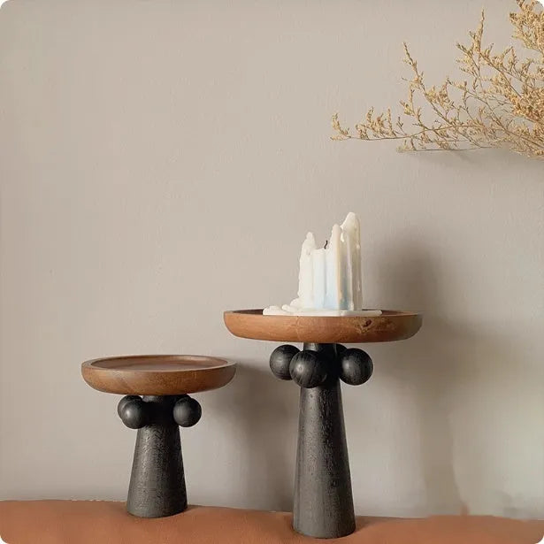 Round high-legged wooden tray in modern style holding a candle and perfume bottle for home decor.