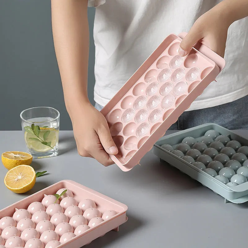 Sky blue 3D round ice ball mould tray with 18 grids next to a pink tray with 33 grids.