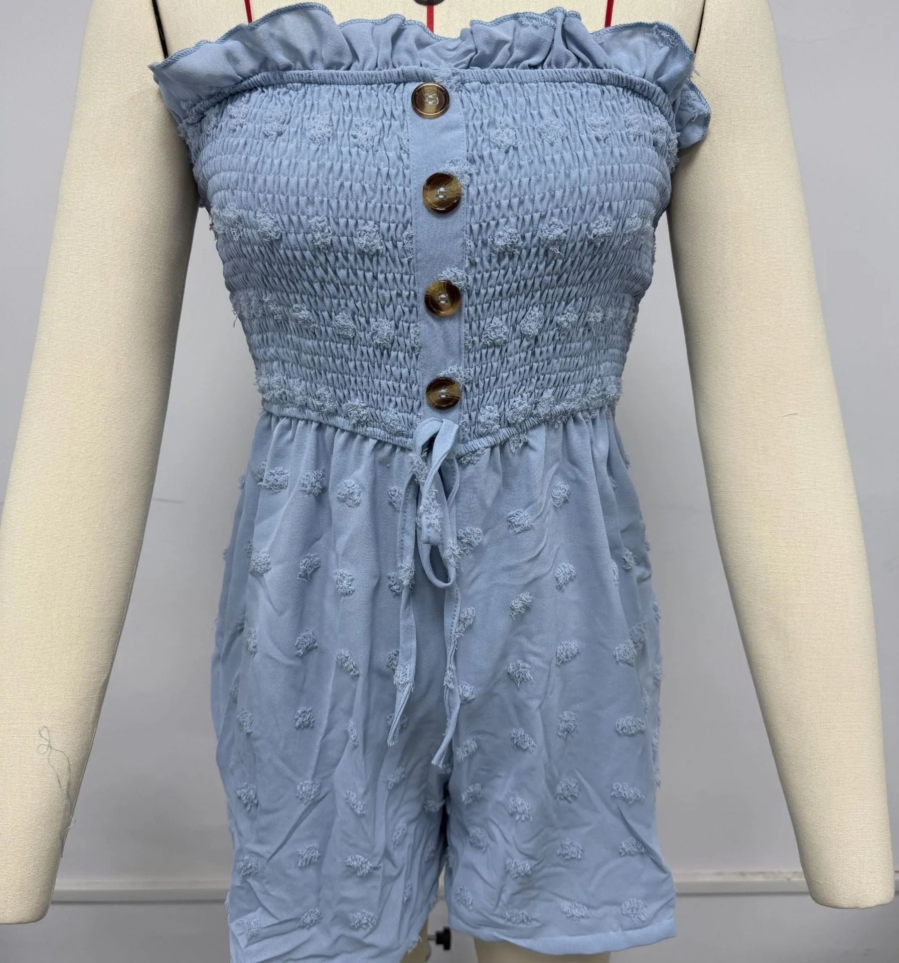 A woman wearing a solid blue off-shoulder sleeveless jumpsuit with a button detail at the front.