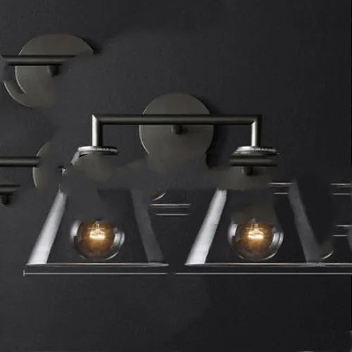 Gold bronze or black wall lamp with triangular transparent glass shade and wrought iron frame for bedside or hallway use