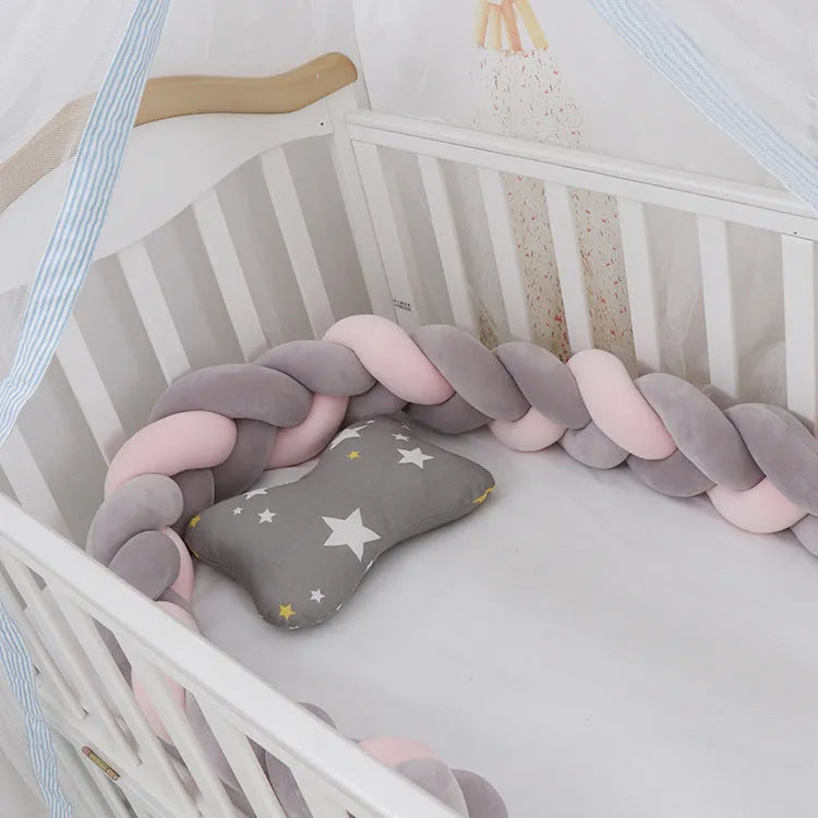 Close-up of a grey braid knot pillow cushion cot bumper fitted around white crib rails.