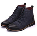 Men's black leather motorcycle ankle boots with side belt buckles and a thick rubber sole on a wooden floor.