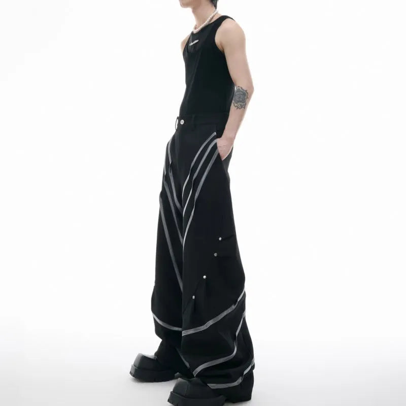 Men's black trousers with pleated detail and metal rivets, showing three-dimensional cut.