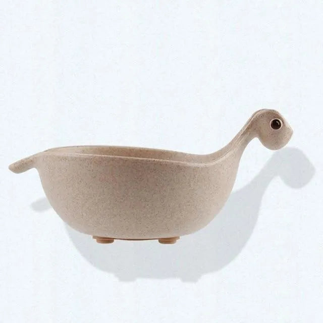 Three wheat straw dinosaur bowls in pink, green, and beige on a kitchen table