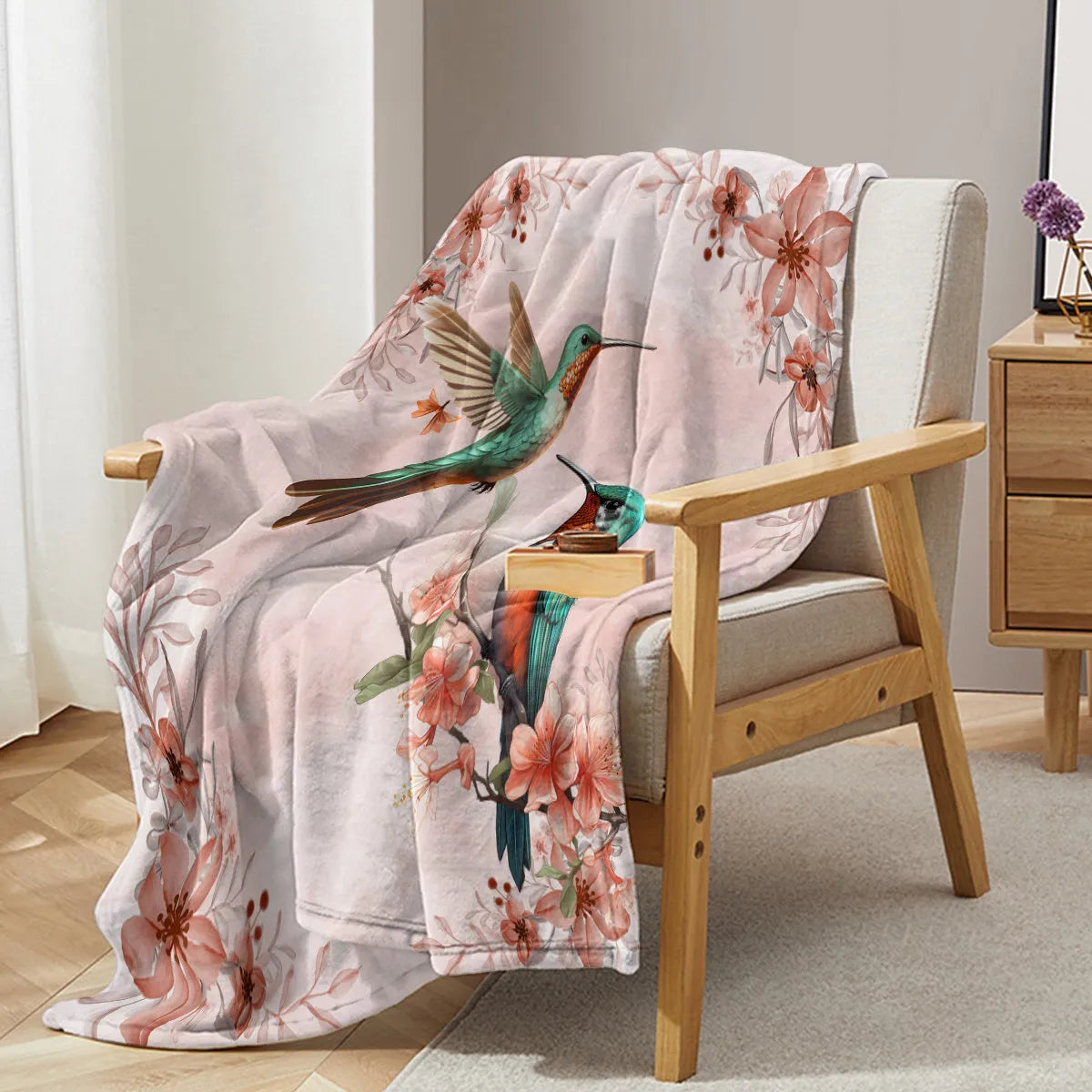 Pink hummingbird floral fleece throw blanket made of soft flannel velvet, folded on a sofa