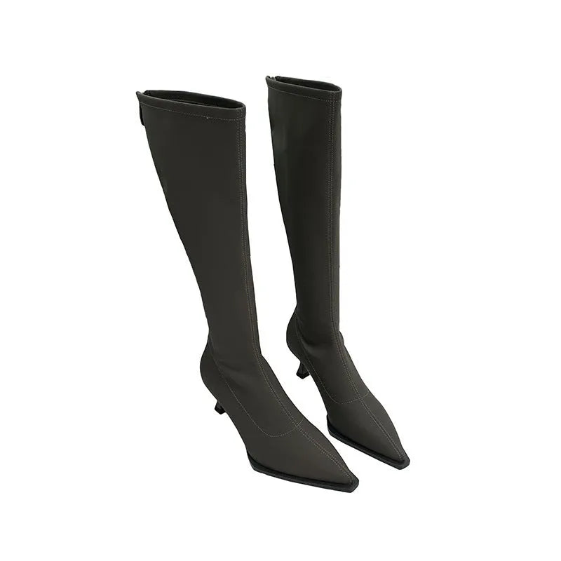 Women's black pointed toe knee-high boots with a stiletto heel and a back zip, shown on a foot.