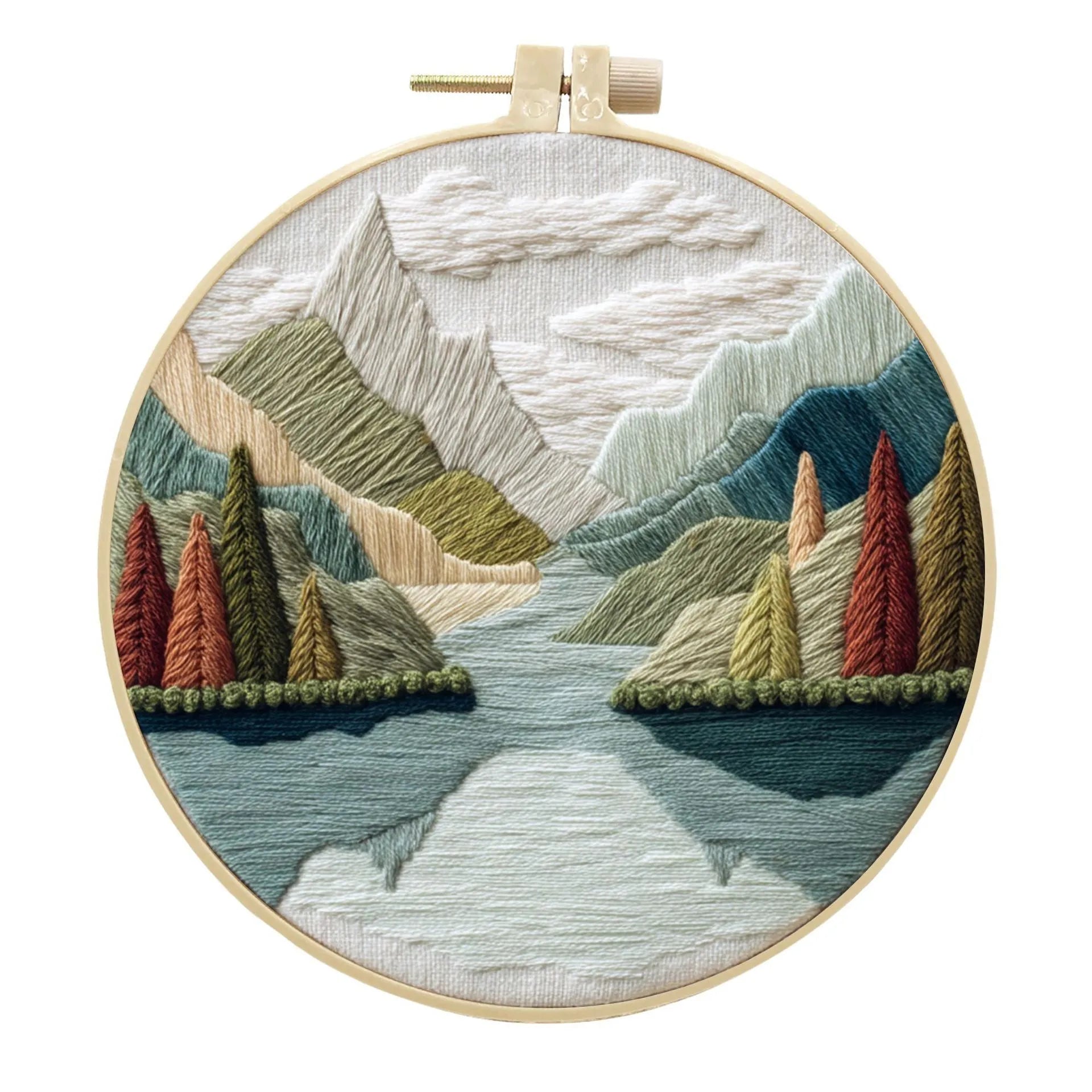 Embroidery DIY kit components: printed landscape fabric, embroidery hoop, coloured threads, and needles laid flat.