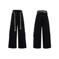 Man wearing dark blue cotton straight-leg trousers with heavy 3D belt stitching and decorative tassel details.
