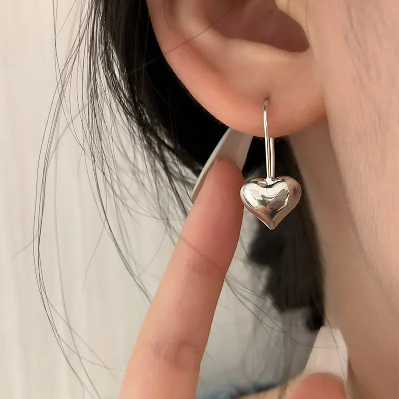 Silver coloured heart-shaped earrings with a glossy three-dimensional design on a white background.