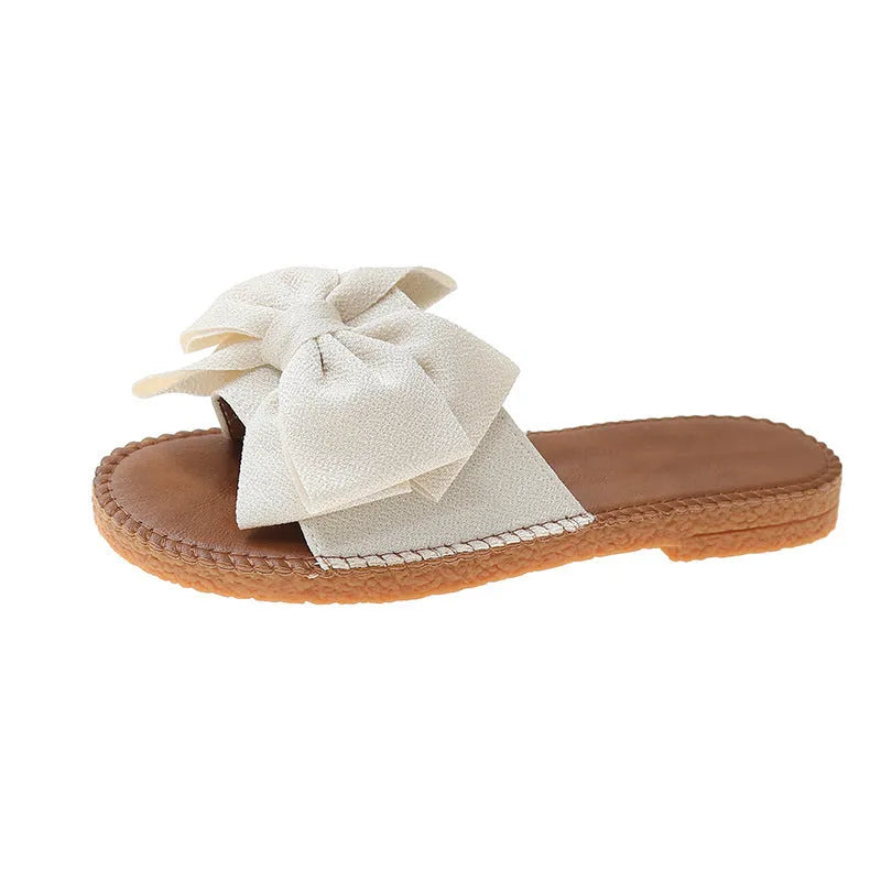 Women's beige slip-on cloth sandals with a bow on the upper and a soft flat rubber sole.