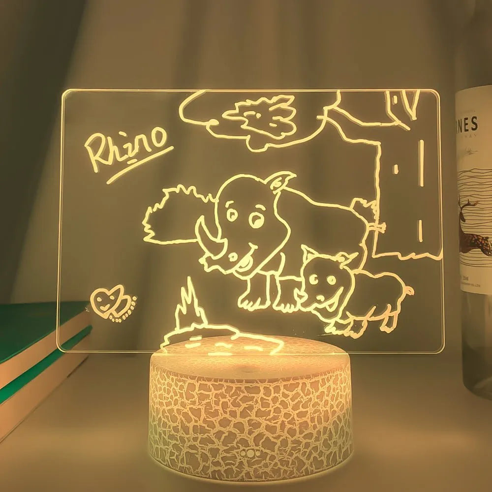 Black 3D acrylic message board night light with remote control and stylus on desk.