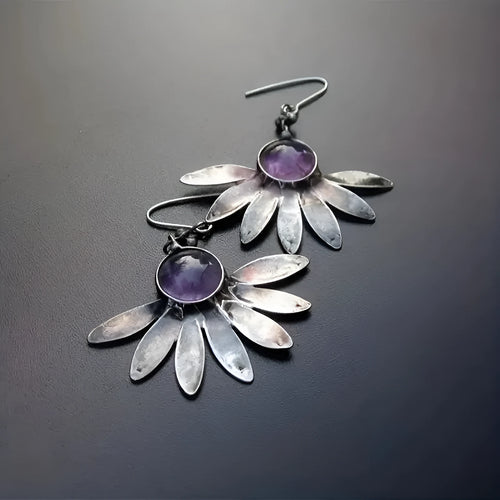 A pair of purple resin bohemian earrings with alloy details and animal or floral modelling on a white background.