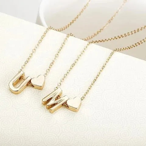 Gold tone peach heart shape pendant with a letter charm on a white background.