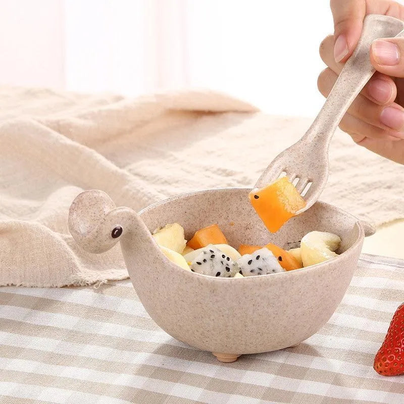 Three wheat straw dinosaur bowls in pink, green, and beige on a kitchen table
