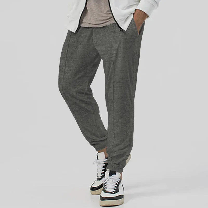 Man wearing grey loose tapered track sweatpants with a micro-elastic cotton blend fabric.