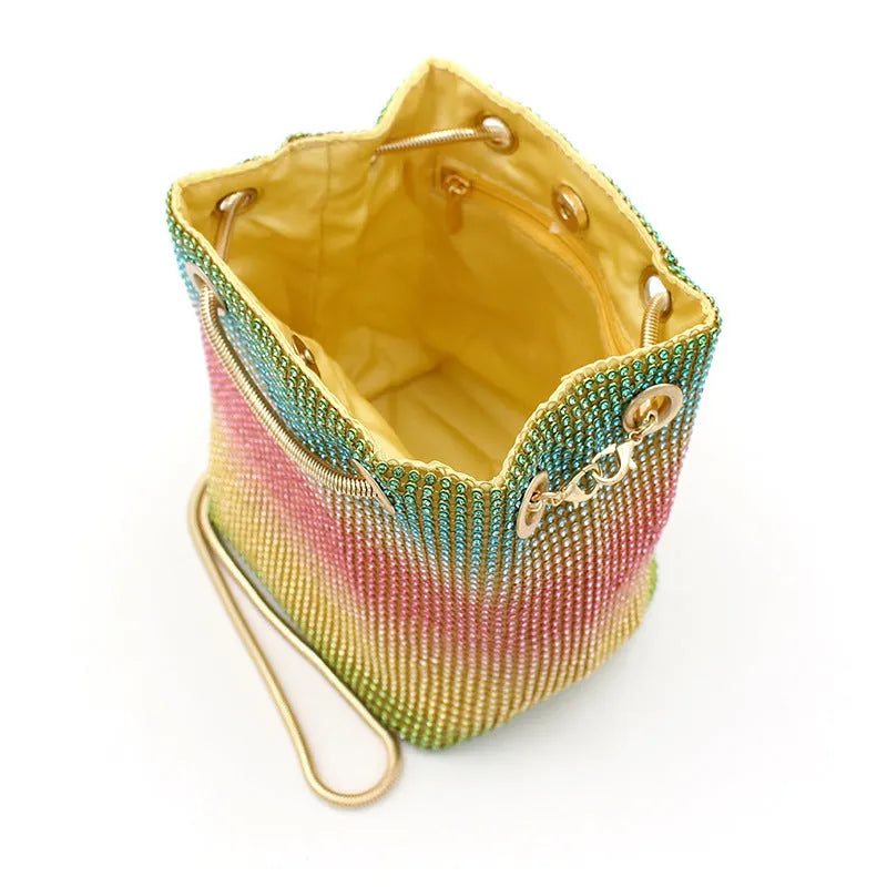 Soft rainbow rhinestone bucket handbag with adjustable long strap on a neutral background.