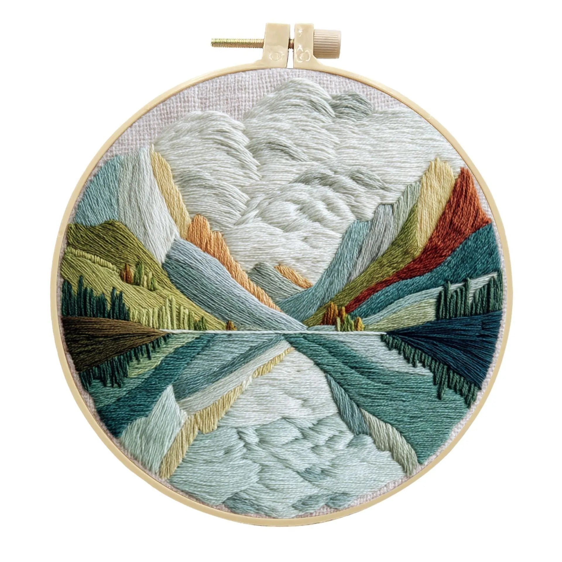 Embroidery DIY kit components: printed landscape fabric, embroidery hoop, coloured threads, and needles laid flat.