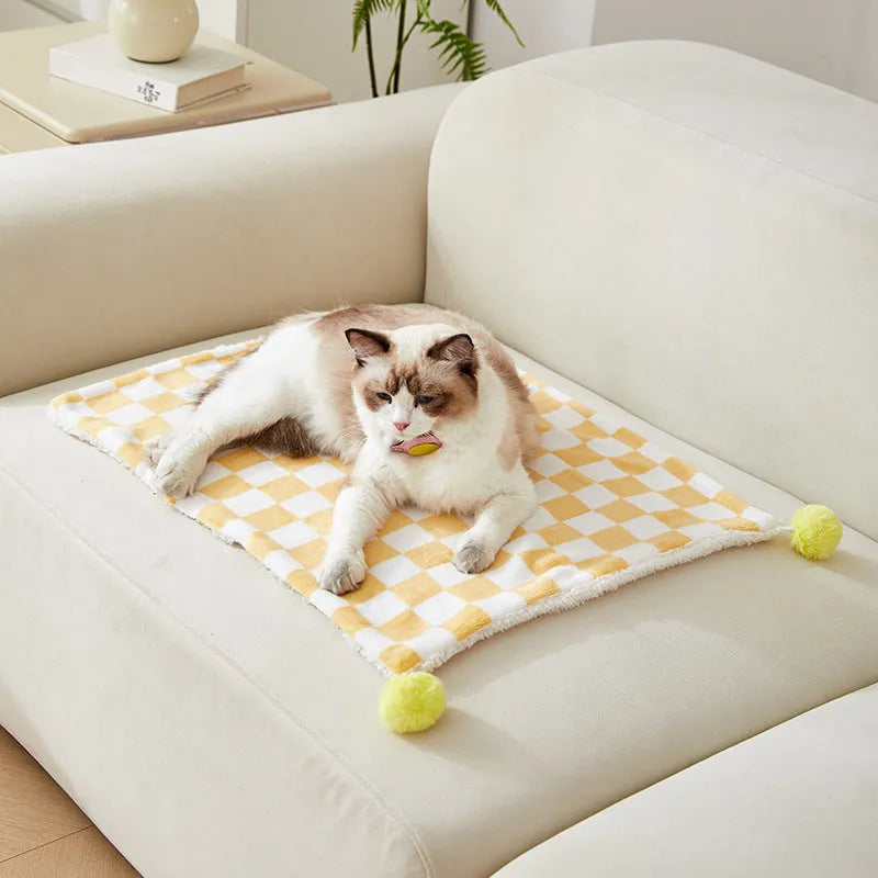 Green plaid pattern fleece pet blanket with a fur ball decoration, shown on a sofa.
